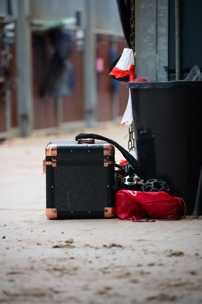 Luxe zwarte poetskoffer met koperen details in de stalgang van de manege